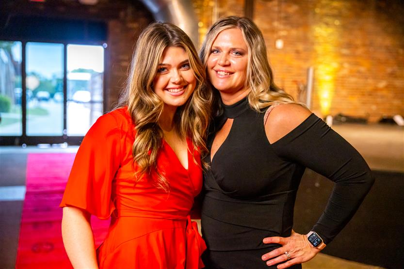 A woman in a red dress and a woman in a black dress smile